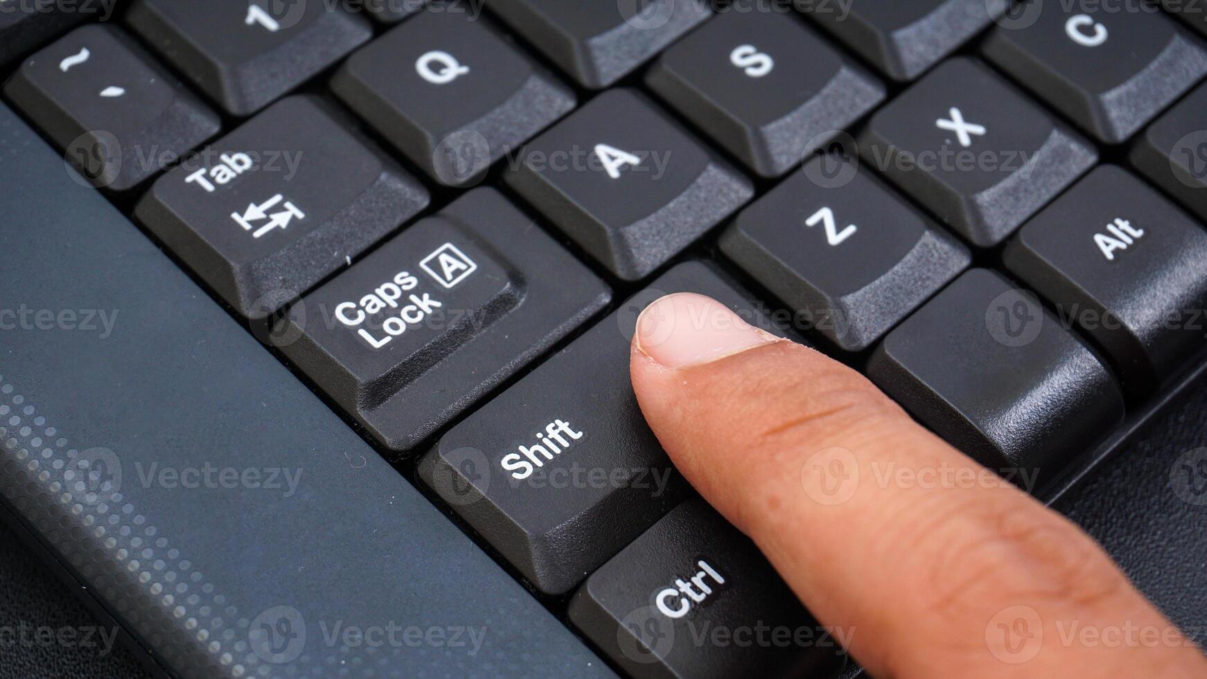 Close up on finger pressing shift button on a computer keyboard isolated on black background photo