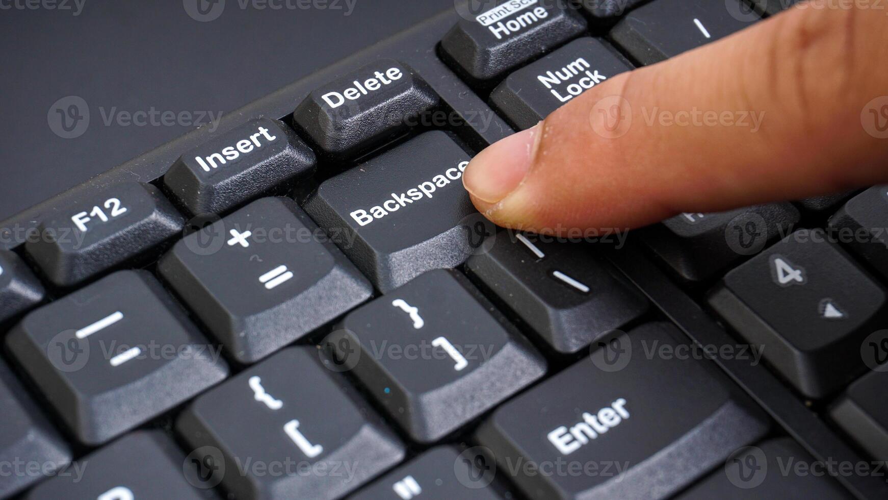 Close up on finger pressing backspace button on a computer keyboard isolated on black background photo