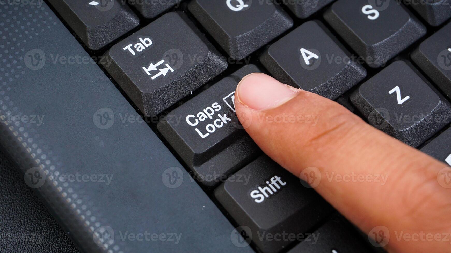 Close up on finger pressing caps lock button on keyboard isolated on black background photo