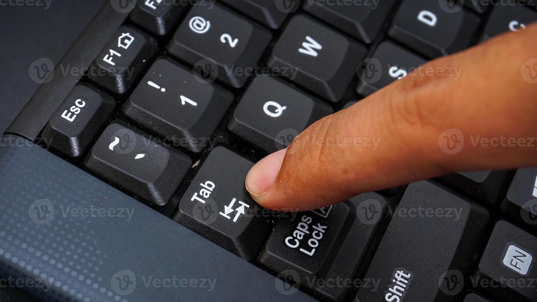Close up on finger pressing tab button on keyboard isolated on black background photo