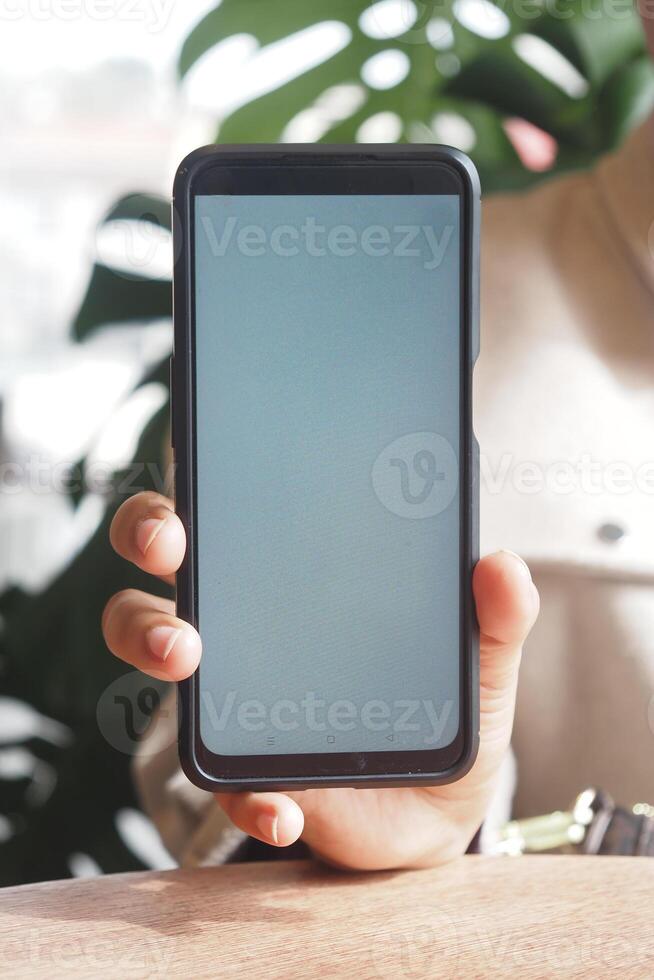 Person holding smartphone in casual indoor setting with greenery photo