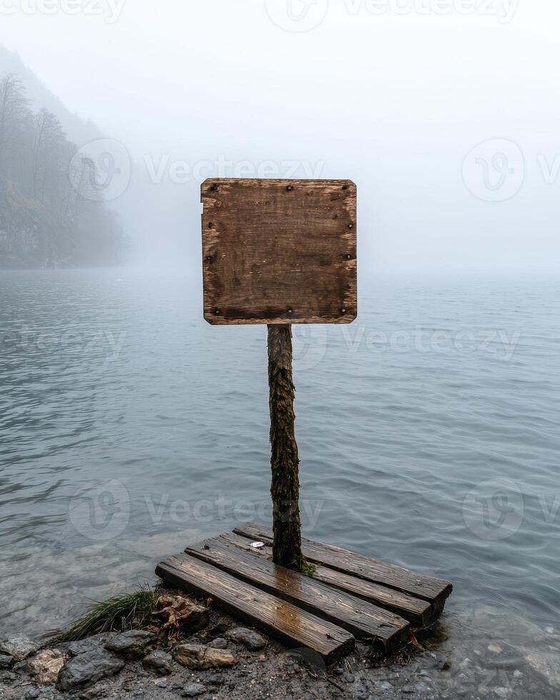 An old wooden sign stands on a platform in a misty lake photo