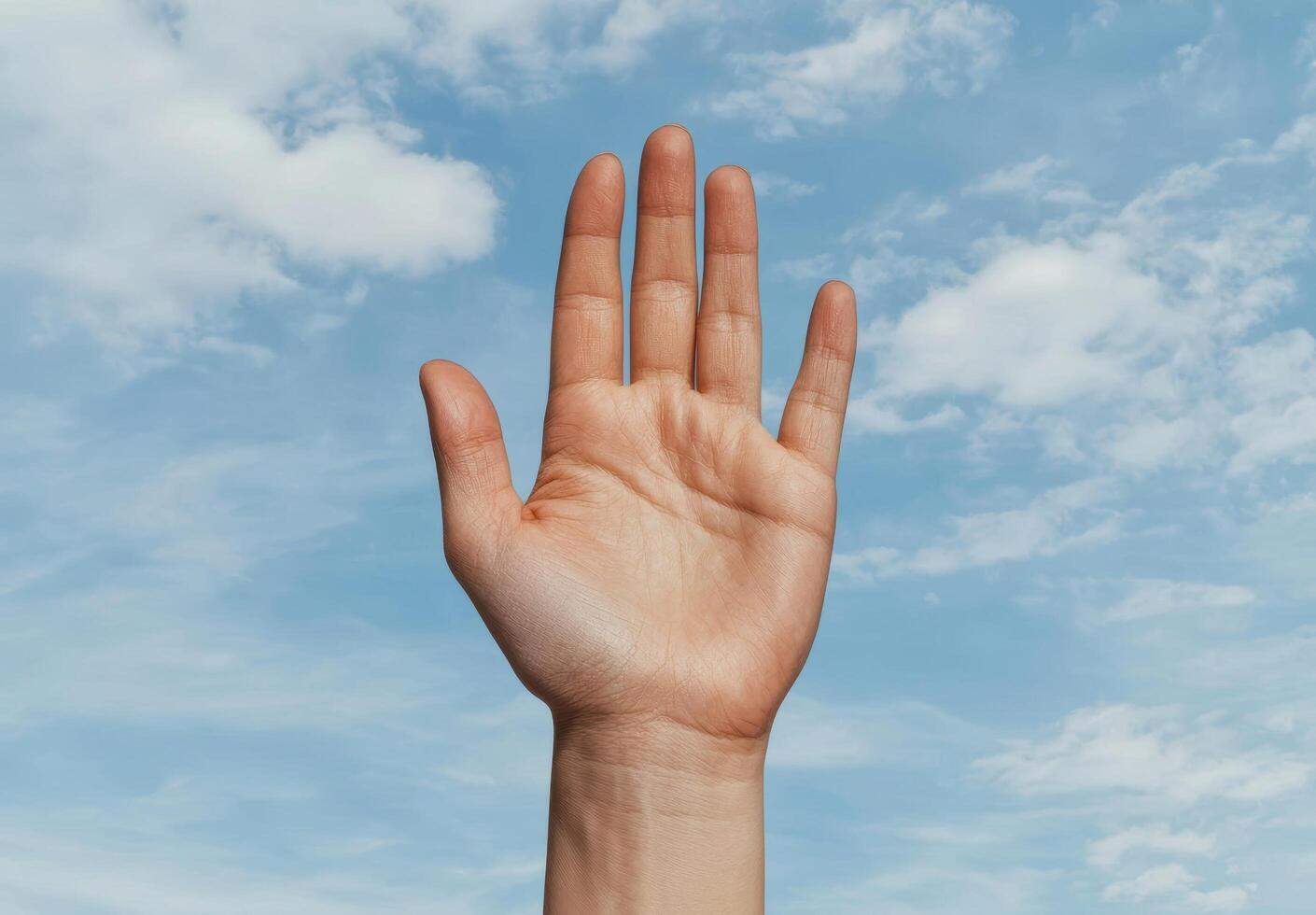 Hand raised in front of a blue sky with clouds photo