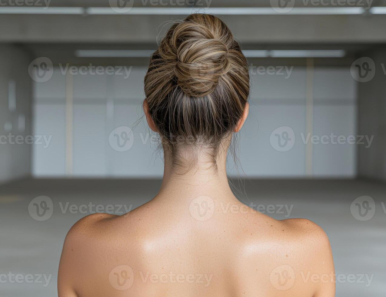Woman with her hair in a bun stands in a large empty room photo