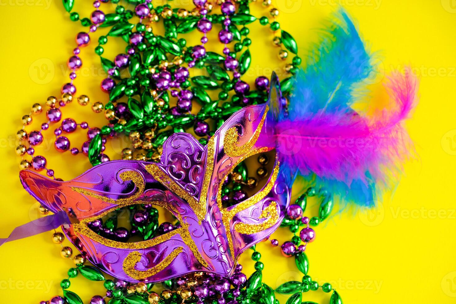 Carnival mask and beads on yellow background. Mardi Gras concept. photo