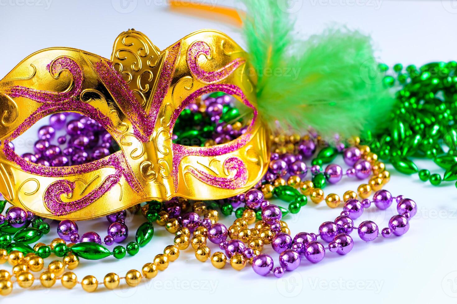 Golden carnival mask and colorful beads on white background. Closeup symbol of Mardi Gras photo