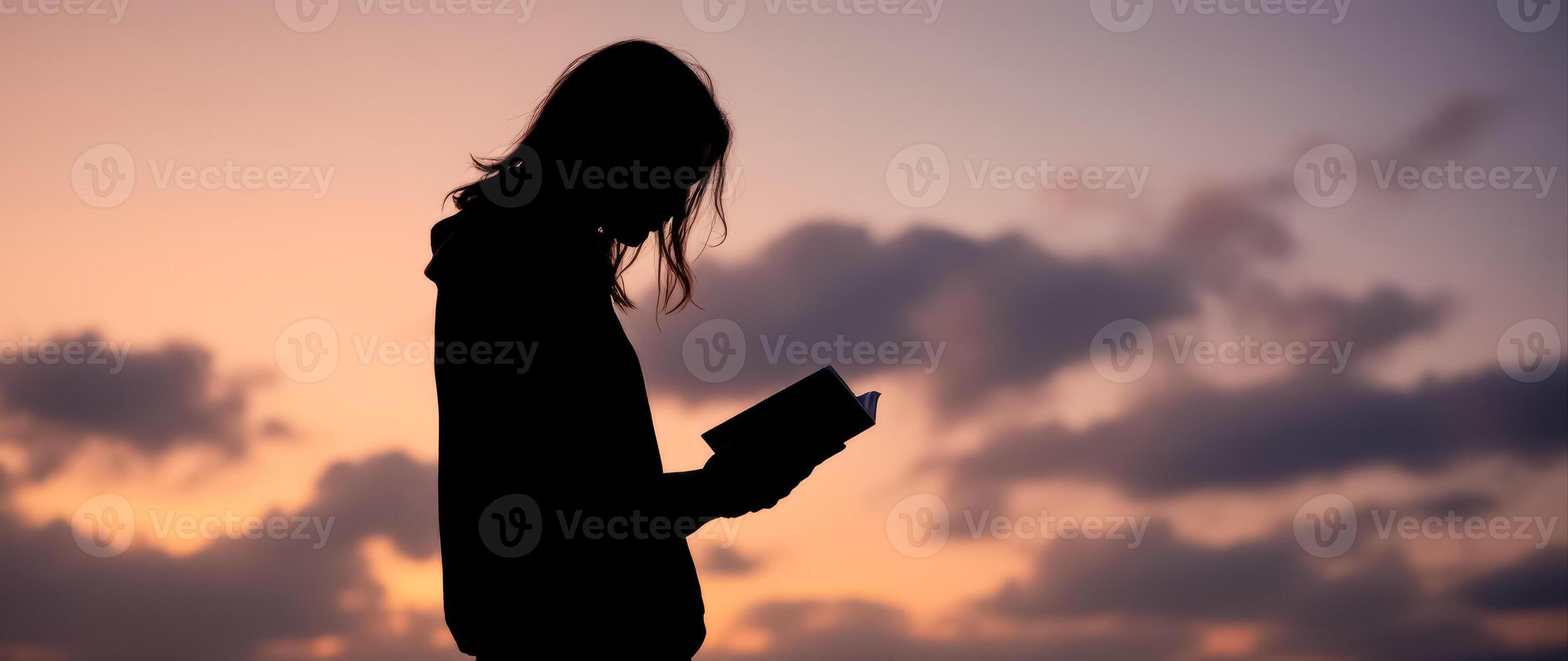 silhouette of a young woman reading a book at sunset photo