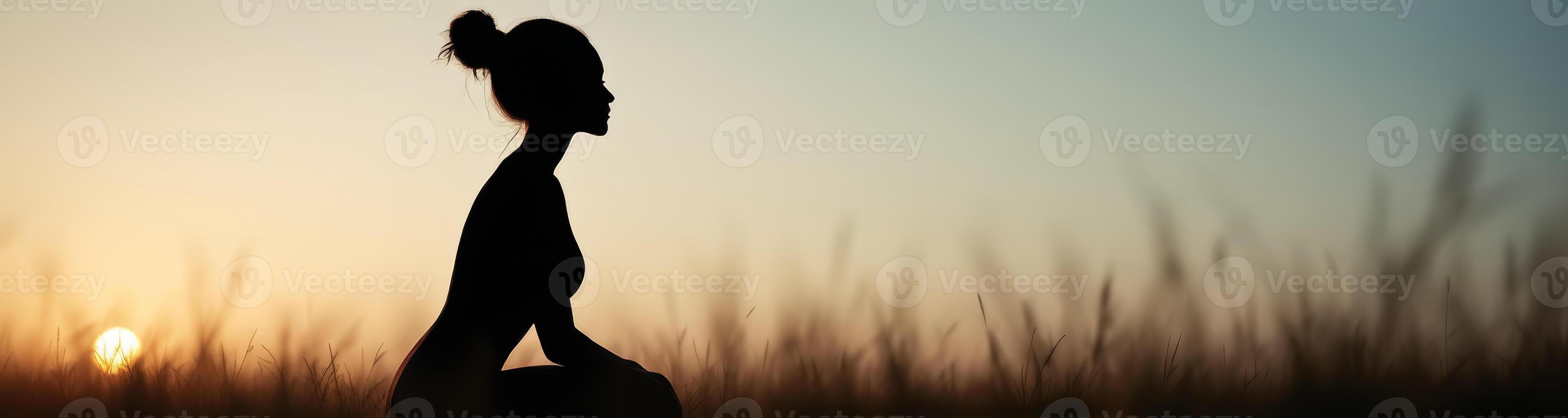 silhouette of a woman sitting in a field at sunset photo