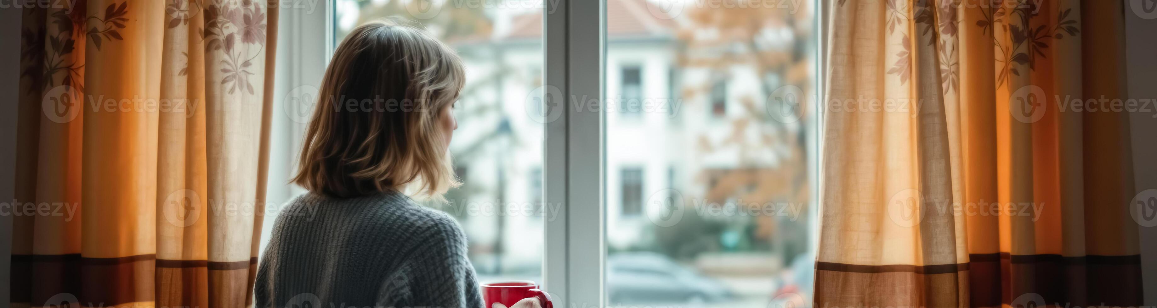 young woman enjoys a warm drink while looking out of a window photo