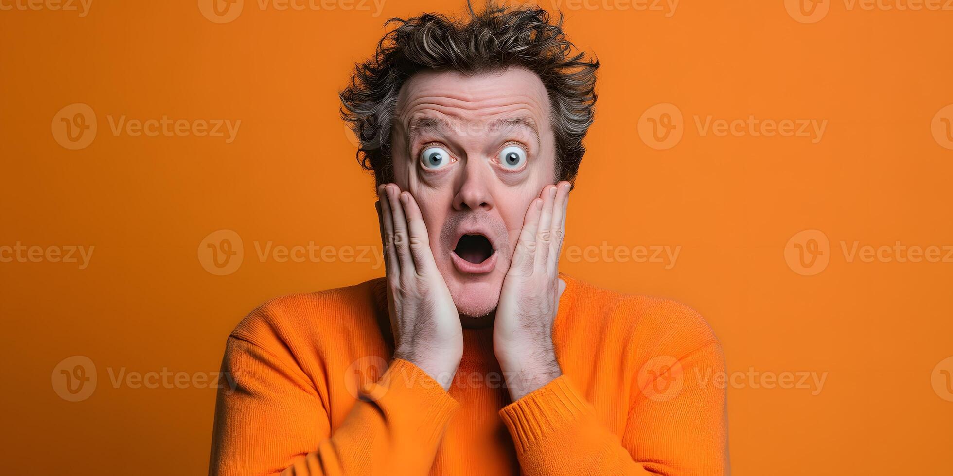 Surprised Man With Wide Eyes Reacting With Hands on Cheeks Against Orange Background photo