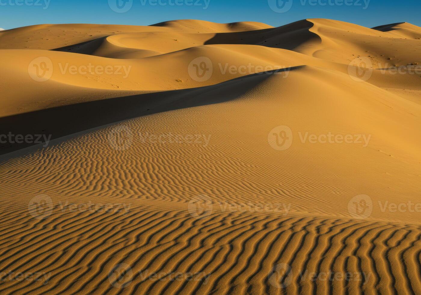 Waves of sand create an endless expanse in the desert under a clear, blue sky. photo
