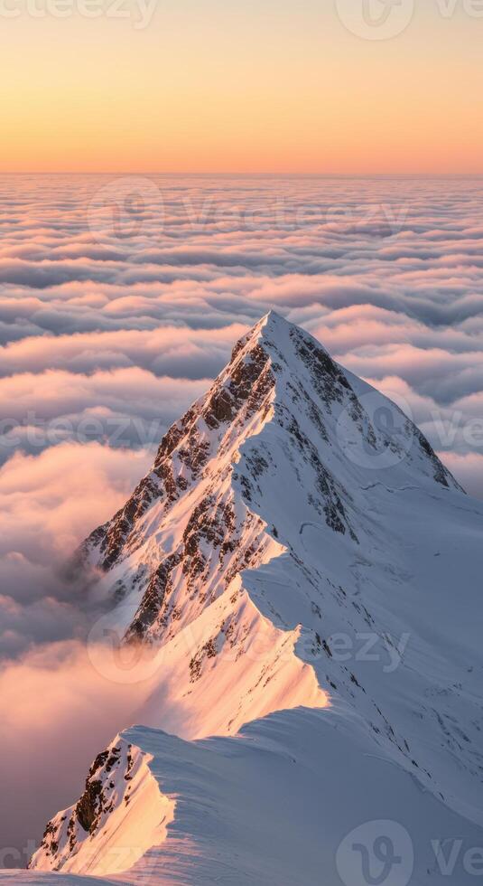 A majestic snow-covered mountain peak rises above a soft blanket of clouds at dusk. photo
