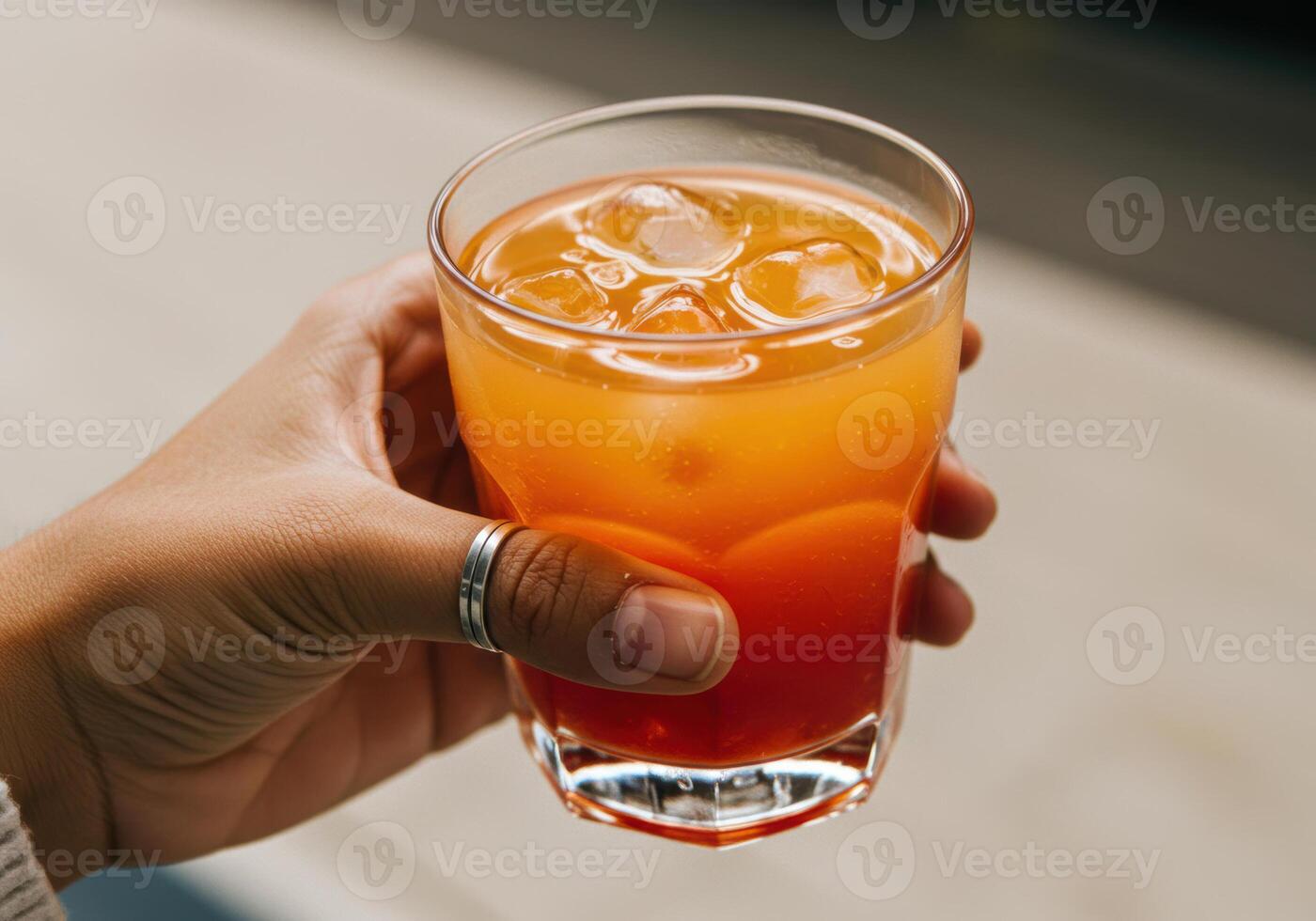 A hand holds a vibrant Tequila Sunrise cocktail, perfect for a sunny day. photo