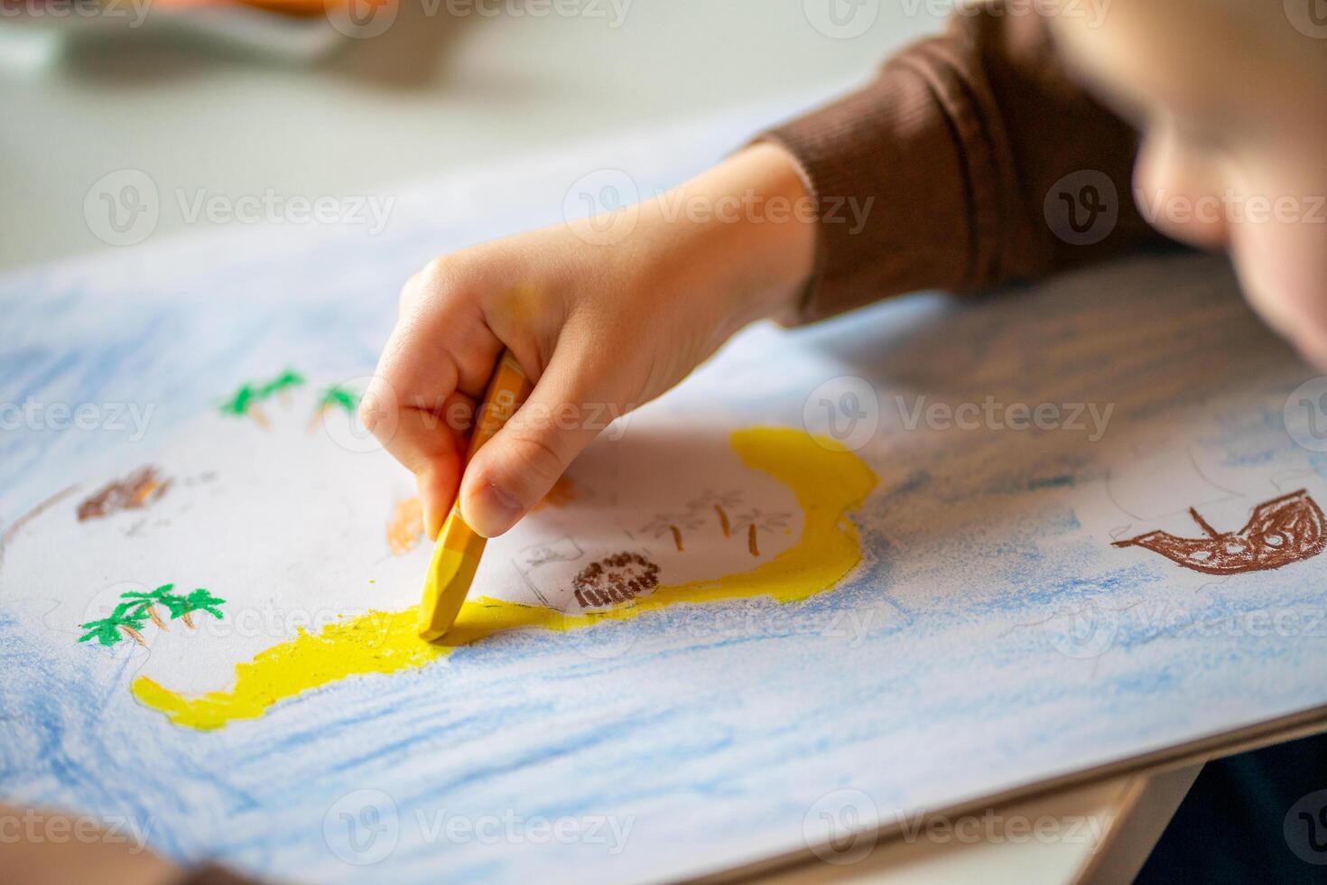 A child in a brown jacket drawing with oil pencils while sitting at the table photo