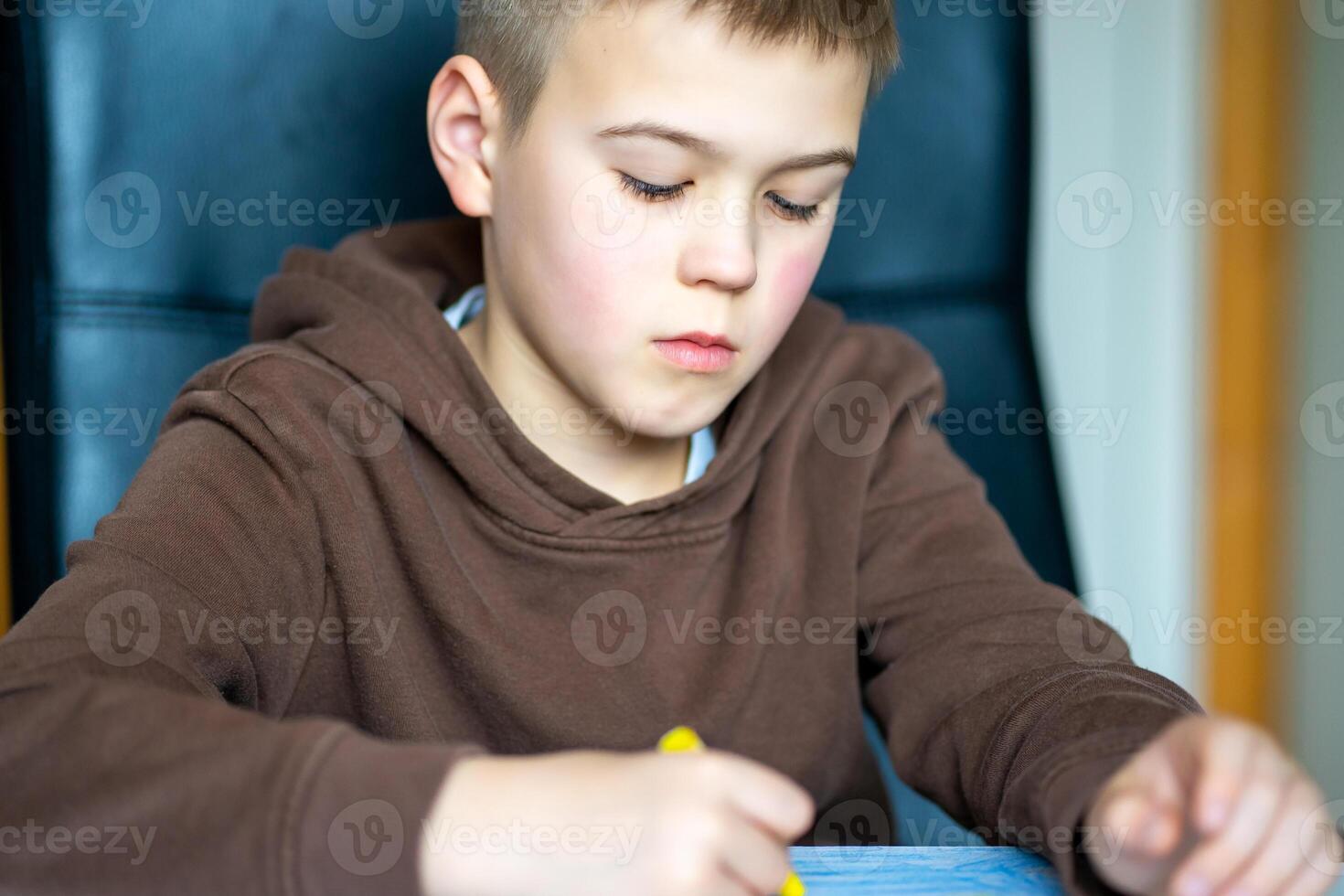 A boy in a brown jacket drawing with oil pencils while sitting at a table photo