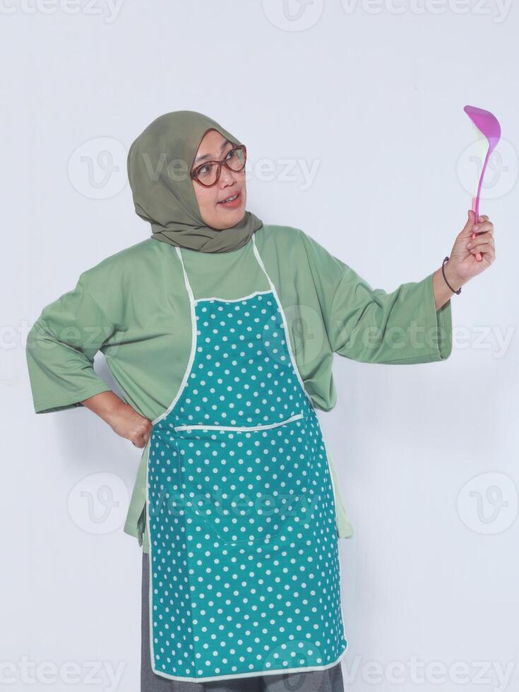 Muslim woman in apron holding a ladle with a curious expression, perfect for culinary and cooking themes photo