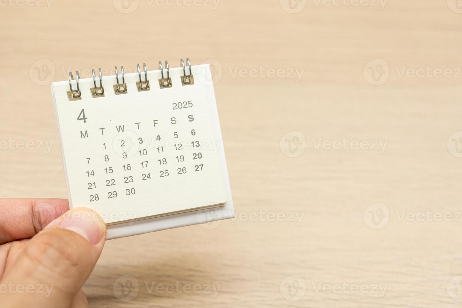 Hand holding mini Calendar for APRIL 2025 background. Calendar concept with 2025 APR calendar on wooden background. Copy Space for text. photo