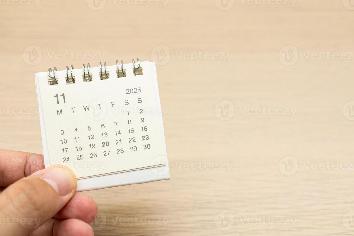 Hand holding mini Calendar for NOVEMBER 2025 background. Calendar concept with 2025 NOV calendar on wooden background. Copy Space for text. photo