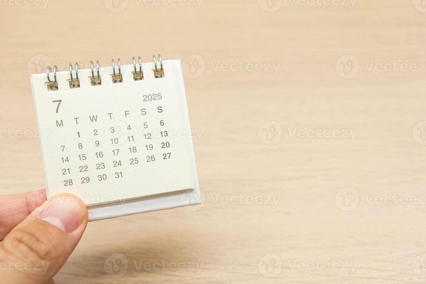 Hand holding mini Calendar for JULY 2025 background. Calendar concept with 2025 JUL calendar on wooden background. Copy Space for text. photo
