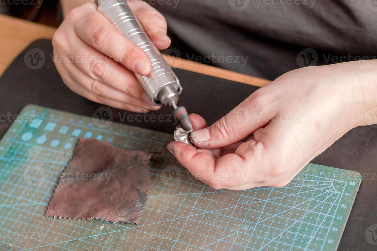 Female hands of jeweler polishing a silver pendant using a rotary tool on a green cutting mat. photo