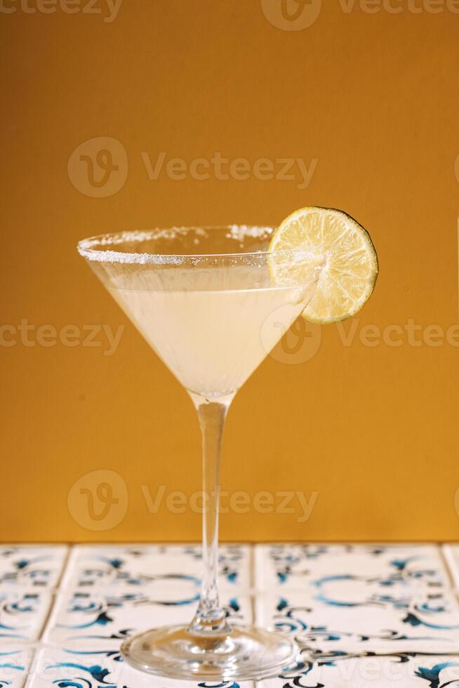 Close-up of an elegant margarita cocktail glass with a slice of lime and sugar on a yellow background. photo