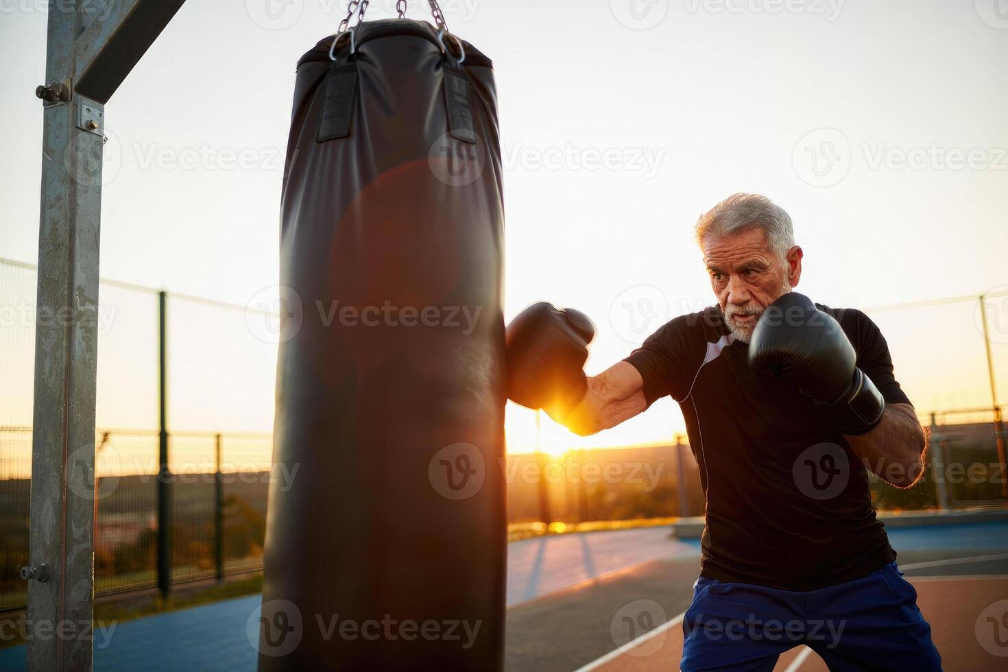 An active senior man is powerfully punching a heavy boxing bag during an intense workout at sunset. photo
