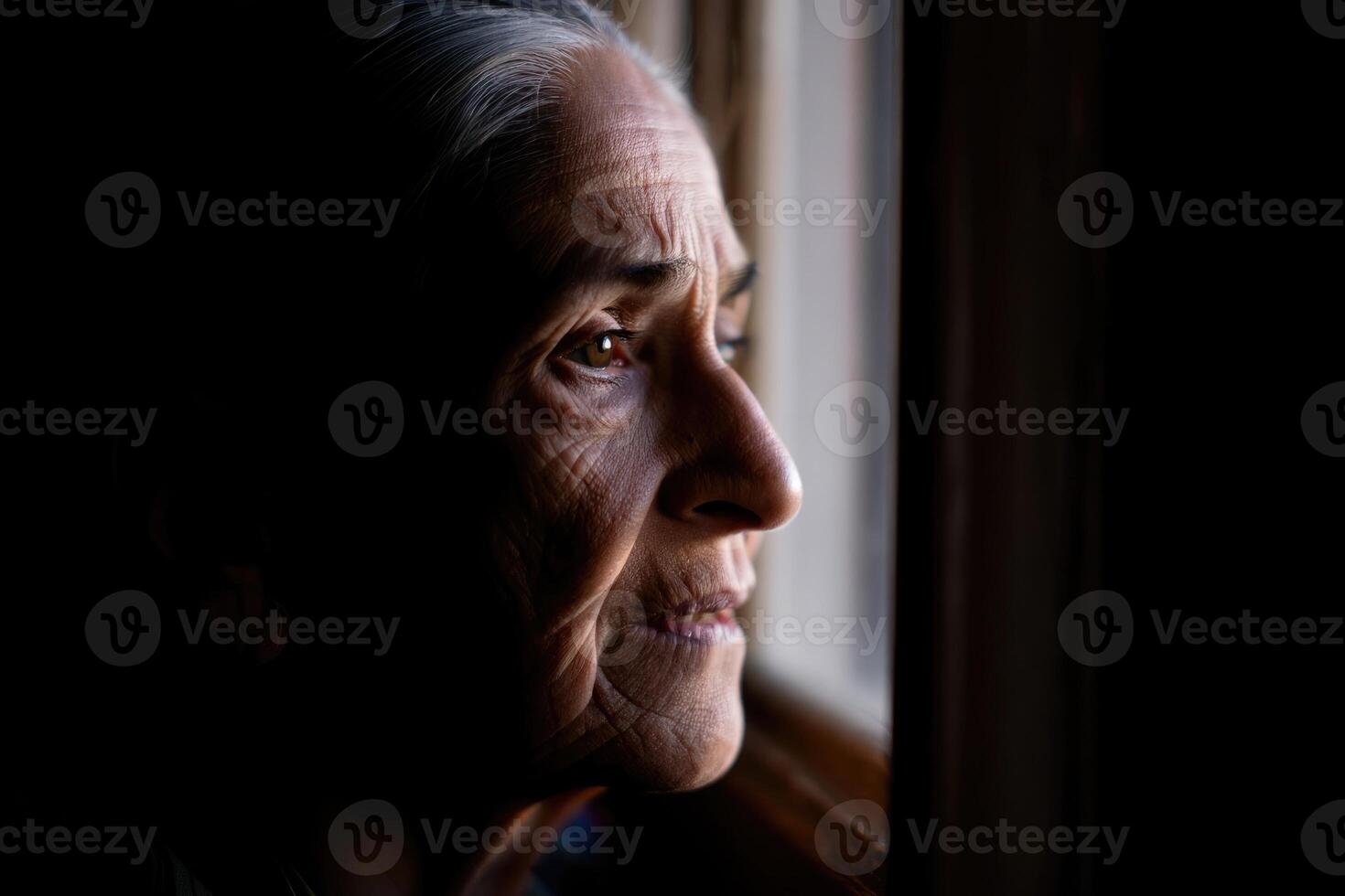 Elderly woman gazing thoughtfully out of a window during the late afternoon light photo