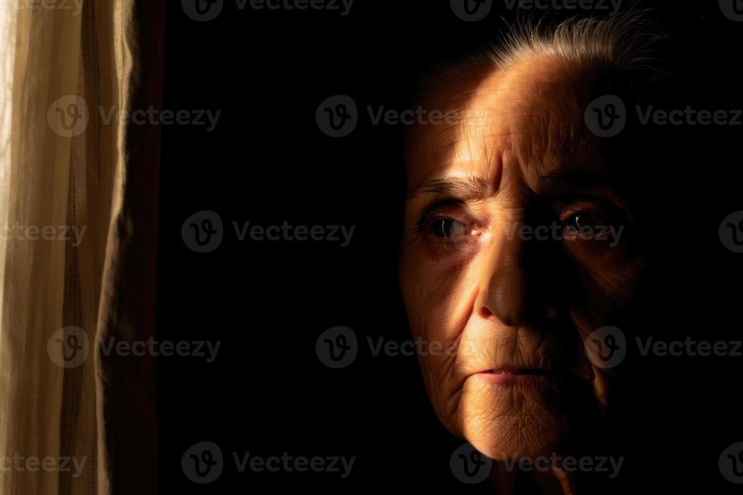 Elderly woman gazes thoughtfully into the light of a dimly lit room during evening hours photo