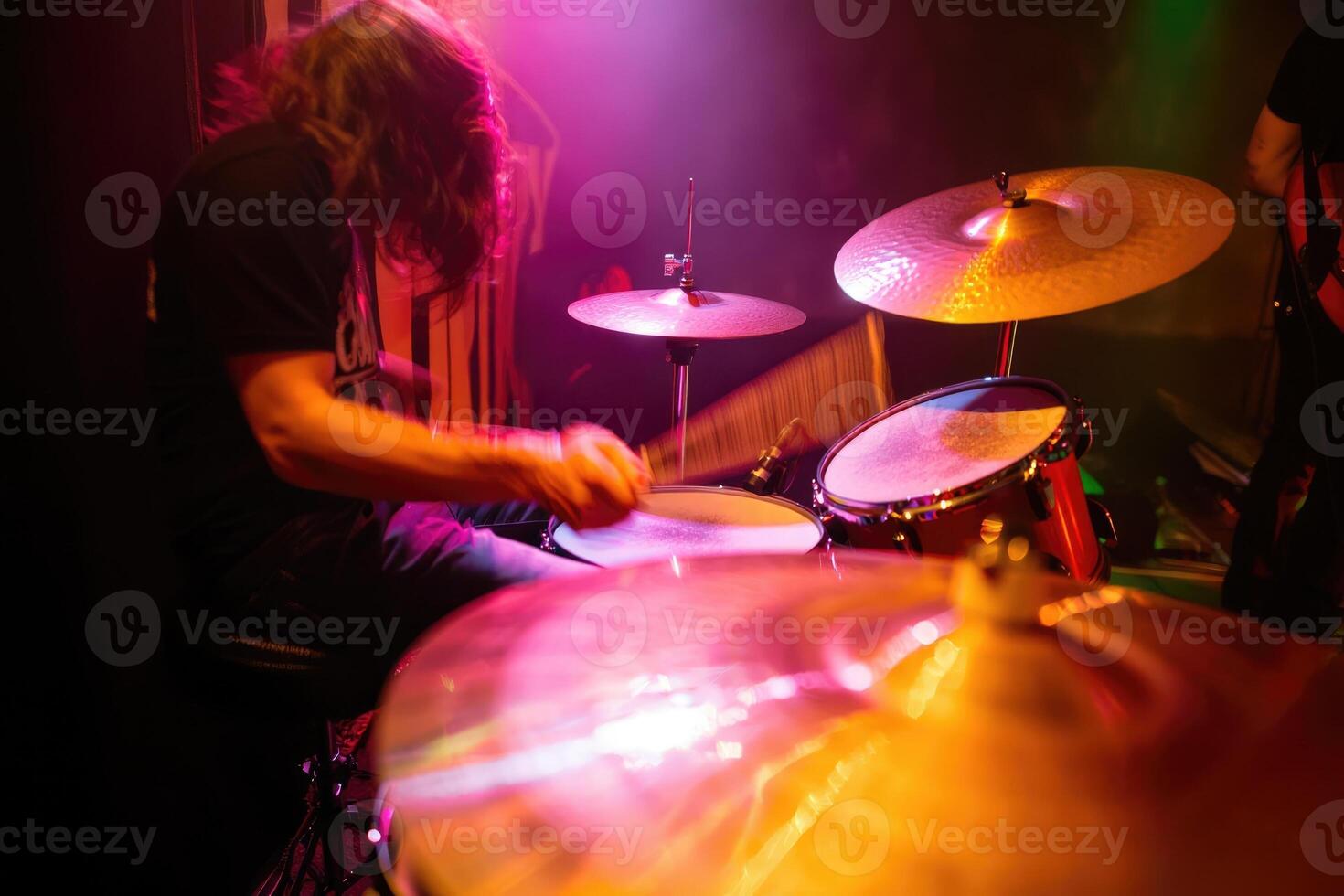 Drummer performing energetically with colorful stage lights illuminating the venue photo