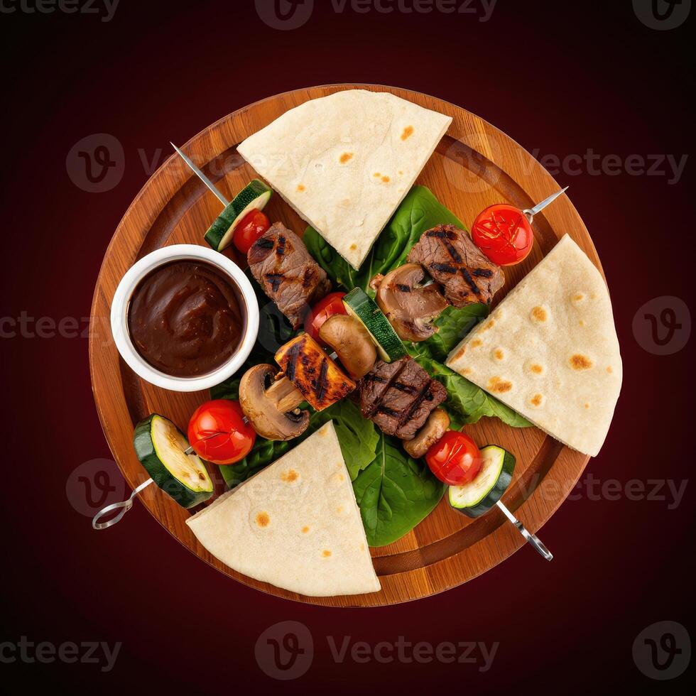 Grilled meat skewer platter with flatbreads and fresh vegetables served on a wooden board photo