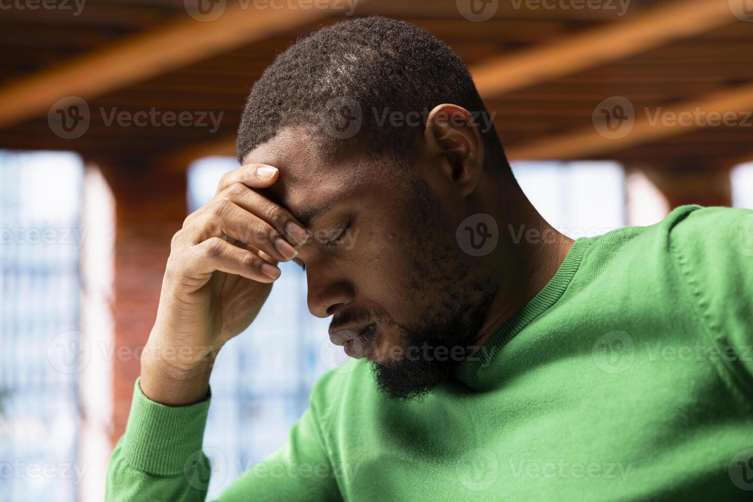 Man at home feeling exhausted from overworking and lack of sleep, suffering from headache. Tired African american person in apartment affected by pain, closing eyes, feeling migraine photo
