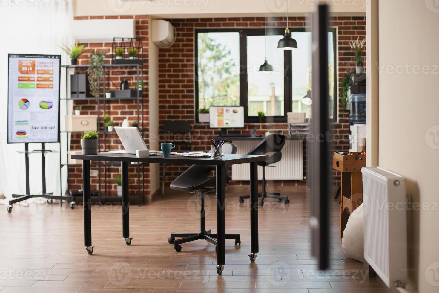 Vacant brick wall room with organized digital devices and furniture prepared for employees to use. Startup company workspace is well arranged with computers and modern office materials. photo