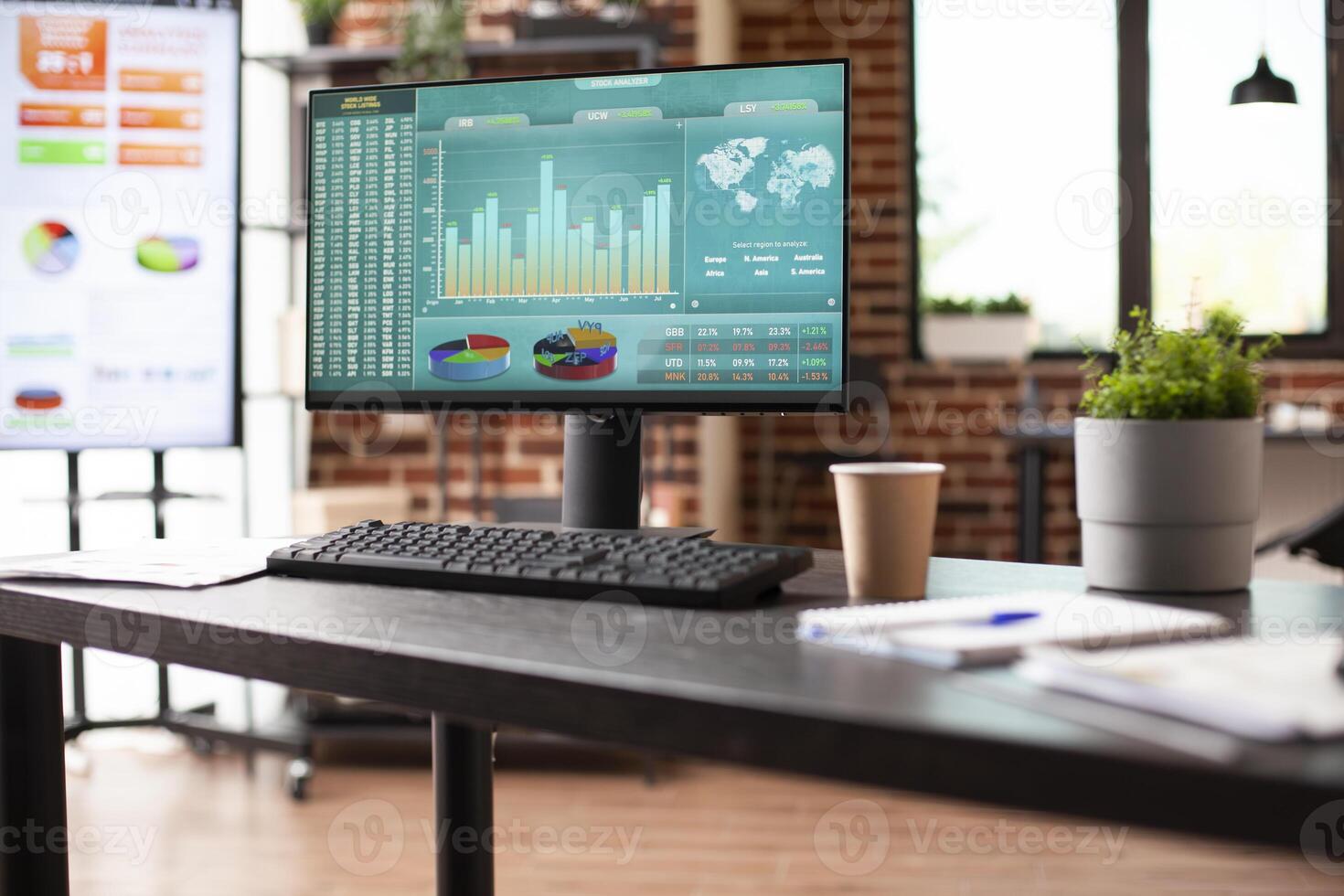 Computer screen displaying marketing strategy research in preparation for a meeting in vacant business office. Brick wall room with nobody is arranged with digital devices showing company analytics. photo