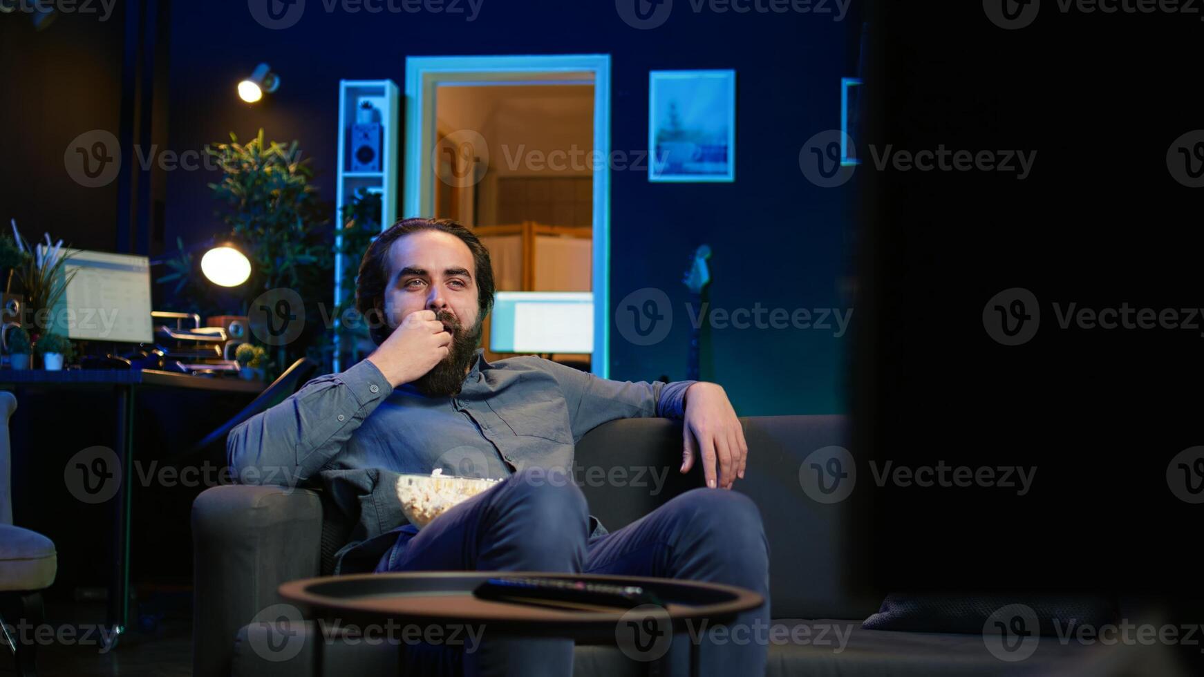 Joyous homeowner using TV to watch comedy films on streaming services, laughing at funny jokes. Radiant man in home theater consuming entertainment, amused by humorous movie scene, camera B photo