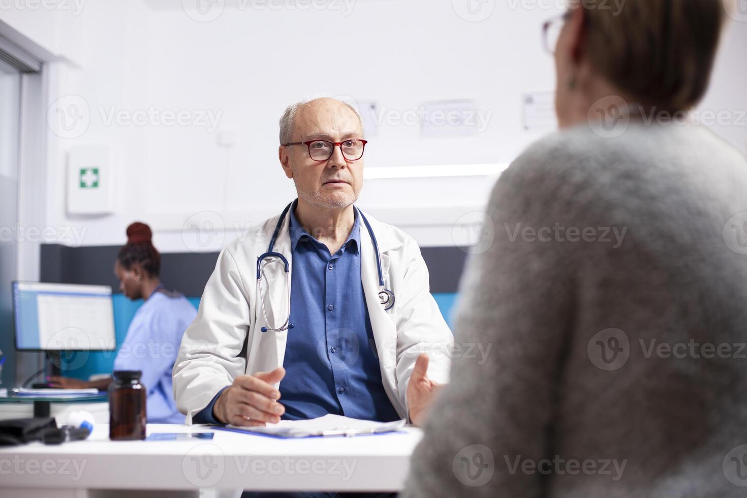 Older male physician having conversation with retired woman during her medical appointment. Senior doctor in lab coat discussing health results and treatment with caucasian female patient in clinic. photo