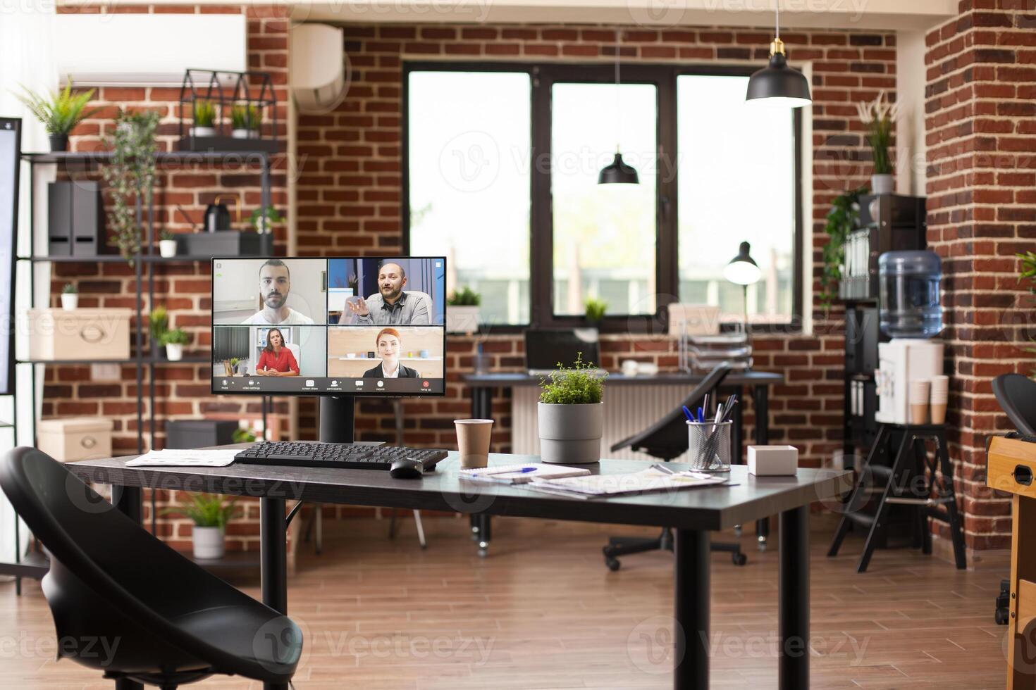 Empty office desk with computer screen displaying group virtual meeting in progress. Videoconference call of caucasian people on desktop monitor in spacious startup workspace with modern furniture. photo