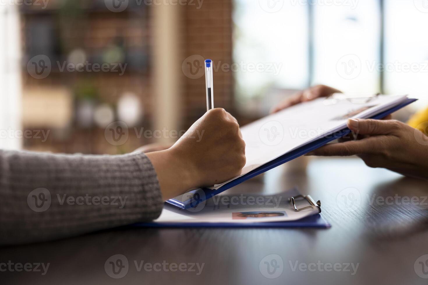 Closeup of an individual signing a document, completing recruitment process in startup company. Selective focus of a person holding a pen and writing on a clipboard at an office desk. photo