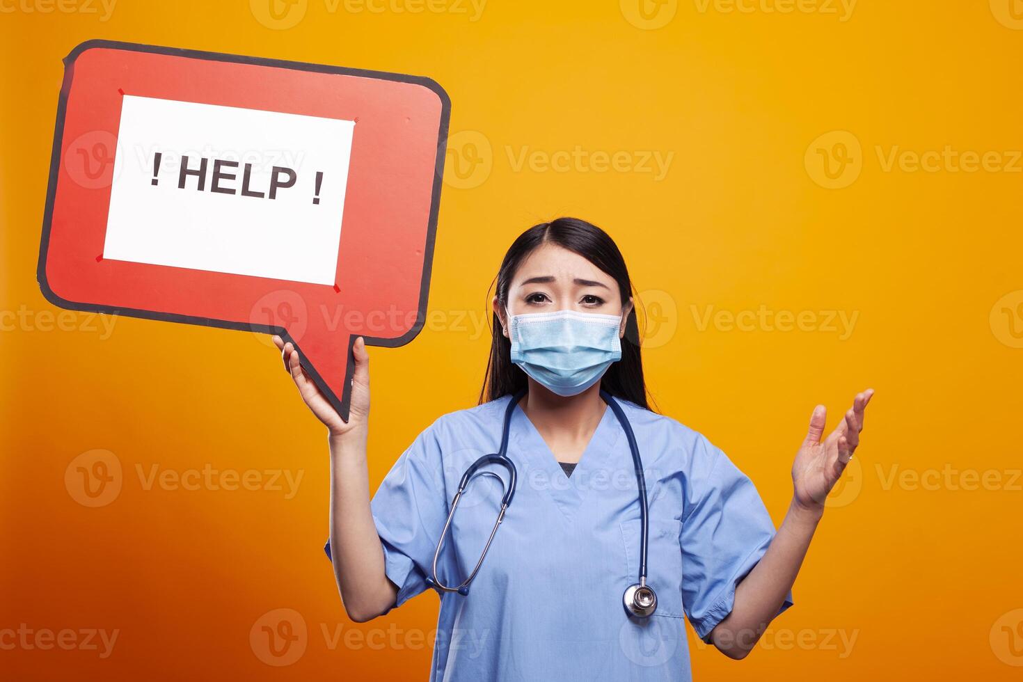 Asian female nurse wearing scrubs and a face mask, holding a help speech bubble, looking distressed. Young woman in medical uniform, grasps a red signboard with an urgent message. photo