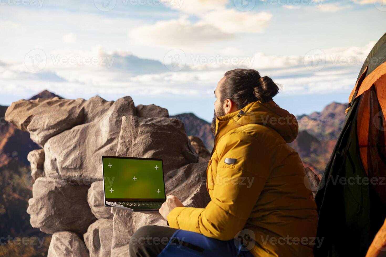 Adventure seeker stands at a mountain peak next to isolated chroma key, looking out at the scenic view that stretches endlessly before him. Fresh air and breathtaking landscape. photo