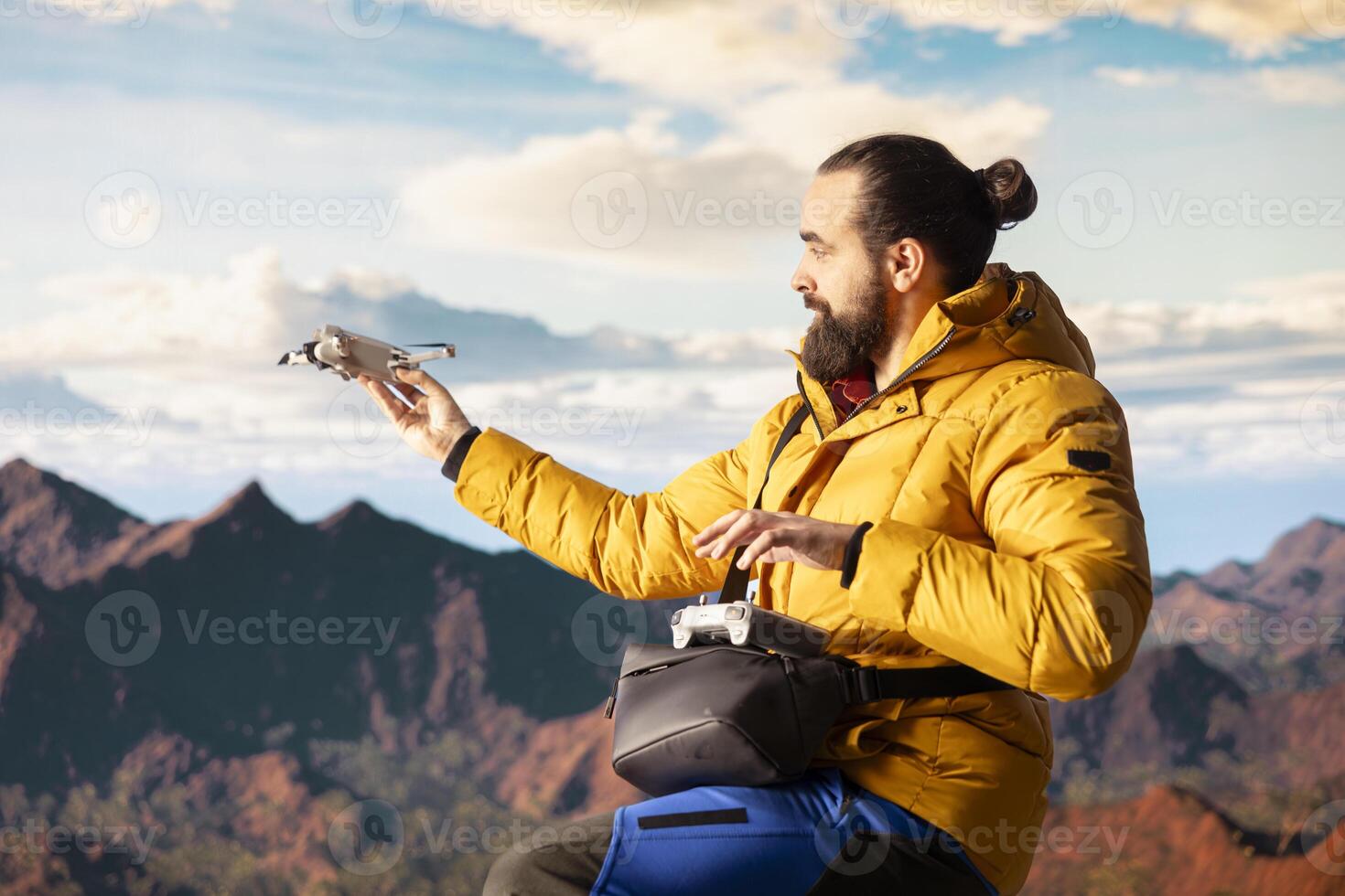 Young explorer influencer recording aerial view vlog with his drone, enjoying the fresh air on mountain range valley. Content creator hiker filming his latest travel vlog, exploration. photo