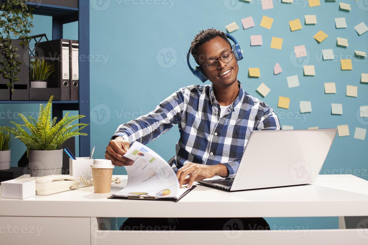 Business advisor at his desk, focused on financial reports, wearing headphones and going through paperwork. Calm accountant reviewing documents and listening to music, flipping through clipboard. photo