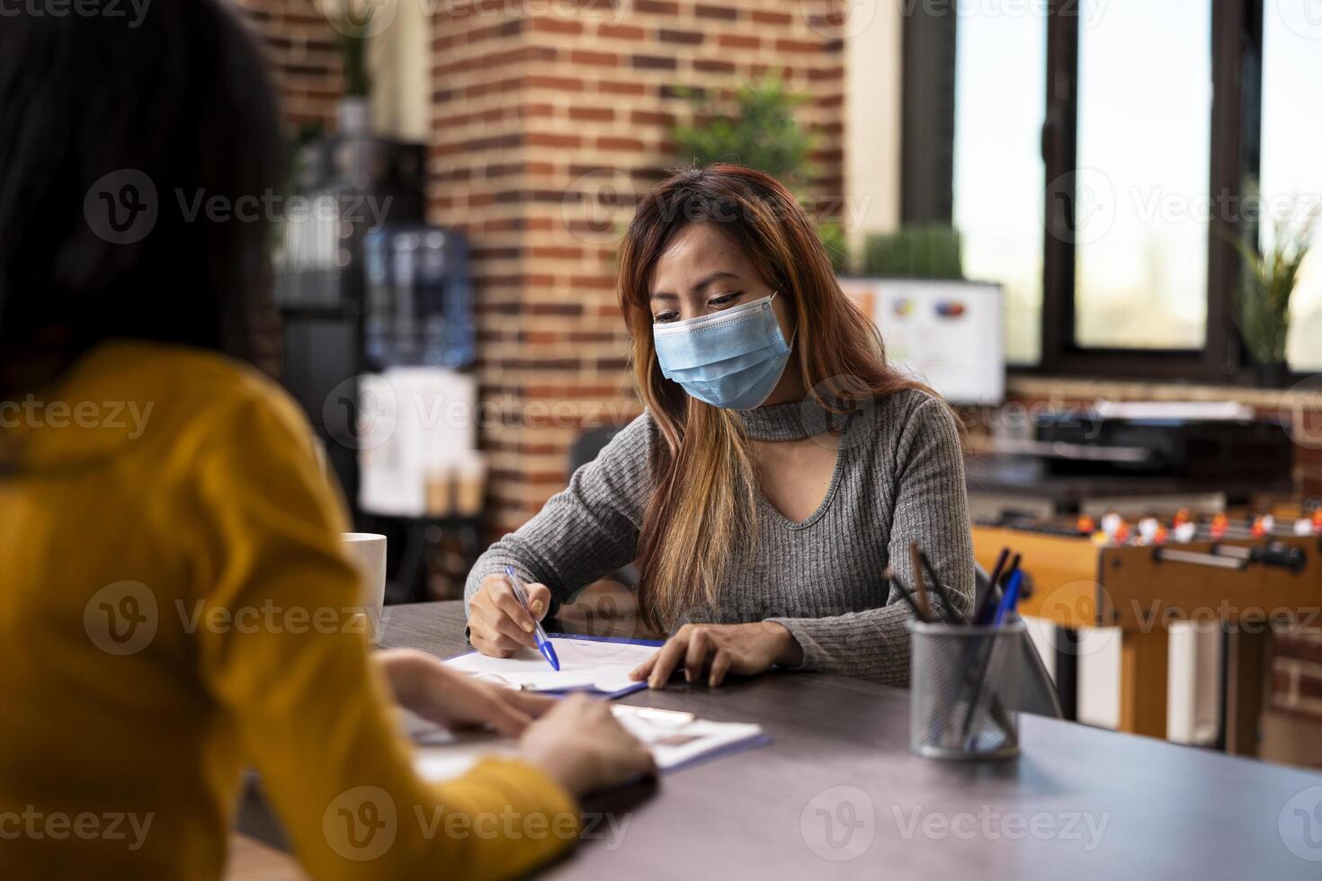 Female business advisor reading document on table and discussing strategy ideas with coworker in modern workspace. Asian recruiter interviewing a woman, asking questions about cv resume on clipboard. photo