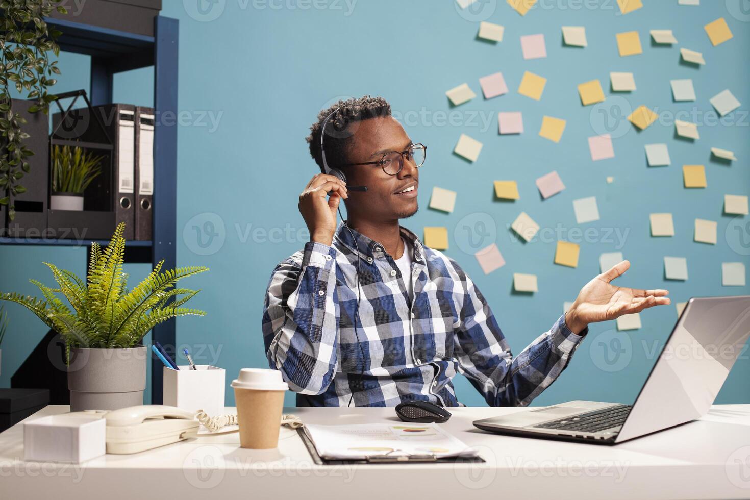 Telemarketer sitting at desk and assisting a client over the phone about application documentation. Company consultant using his laptop and handling a call, providing assistance to the employee. photo