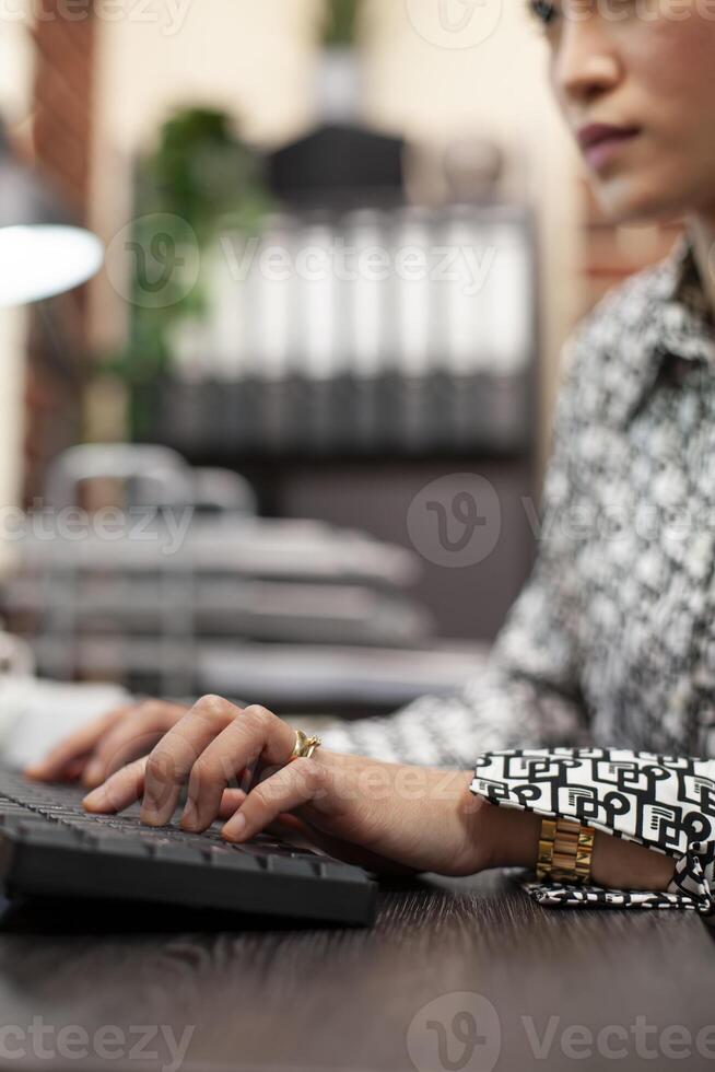 Female professional typing on computer keyboard at a modern office desk. Asian woman busy inputting project details, touching keys to update company financial information on the desktop pc. photo