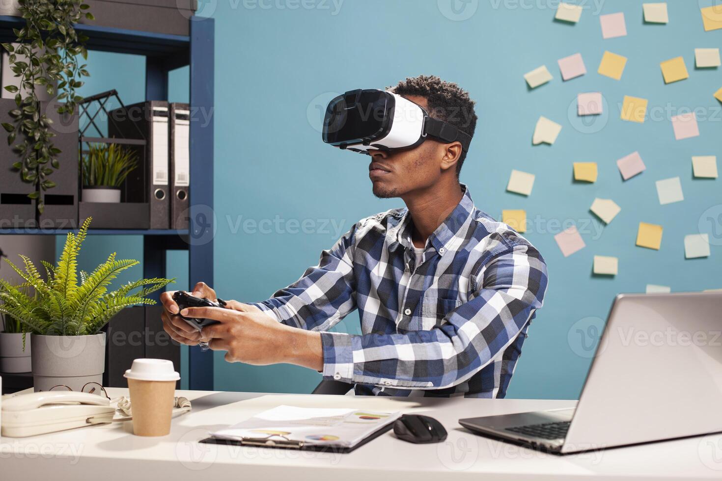 Playful male employee competing in a game using a modern console controller. Startup project manager unwinding with metaverse gaming, using a gamepad and VR headset at his office desk. photo