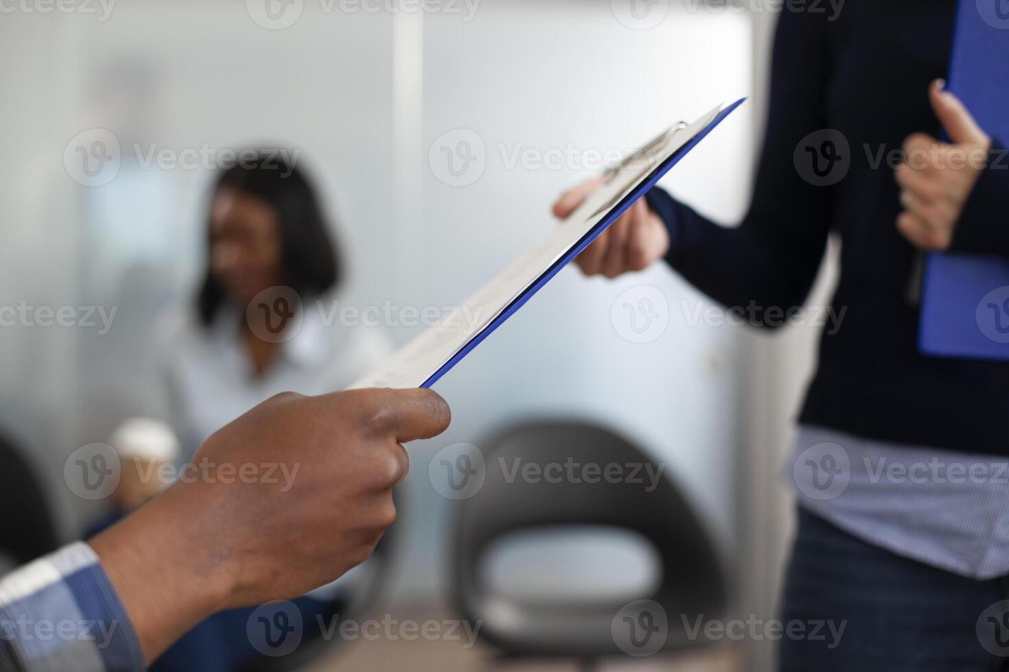 Closeup of multiethnic individuals holding a clipboard in an office lobby. Selective focus of african american job applicant giving a document to a caucasian recruiter in startup company waiting area. photo