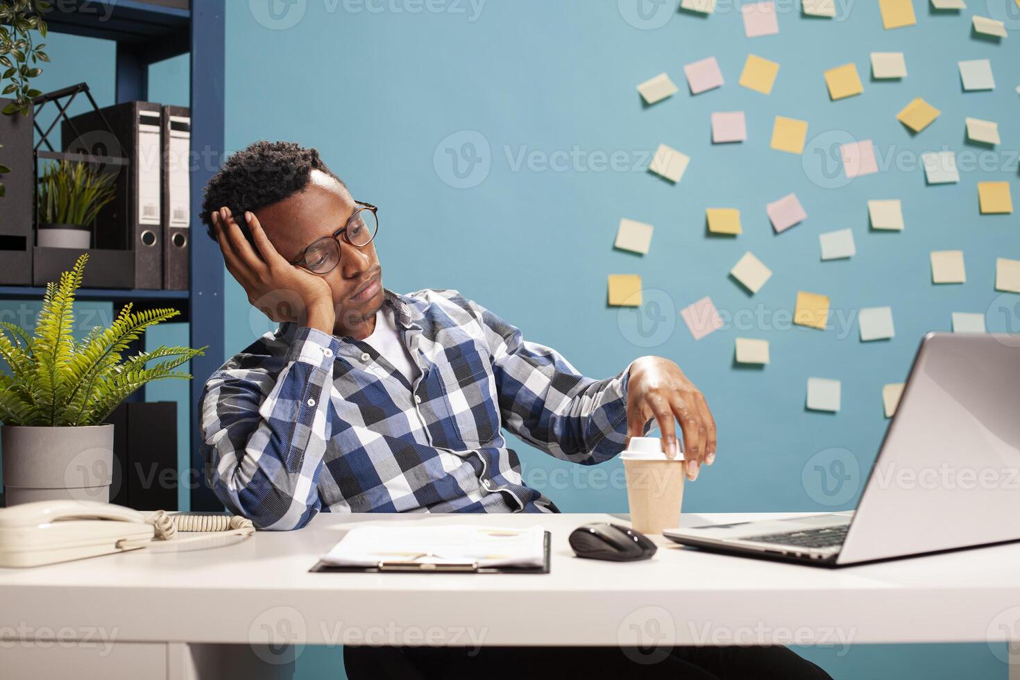 Tired marketing specialist sitting at desk, reviewing key performance indicators on laptop, deep in thought. Exhausted manager resting his head on hand and looking at device screen, online learning. photo