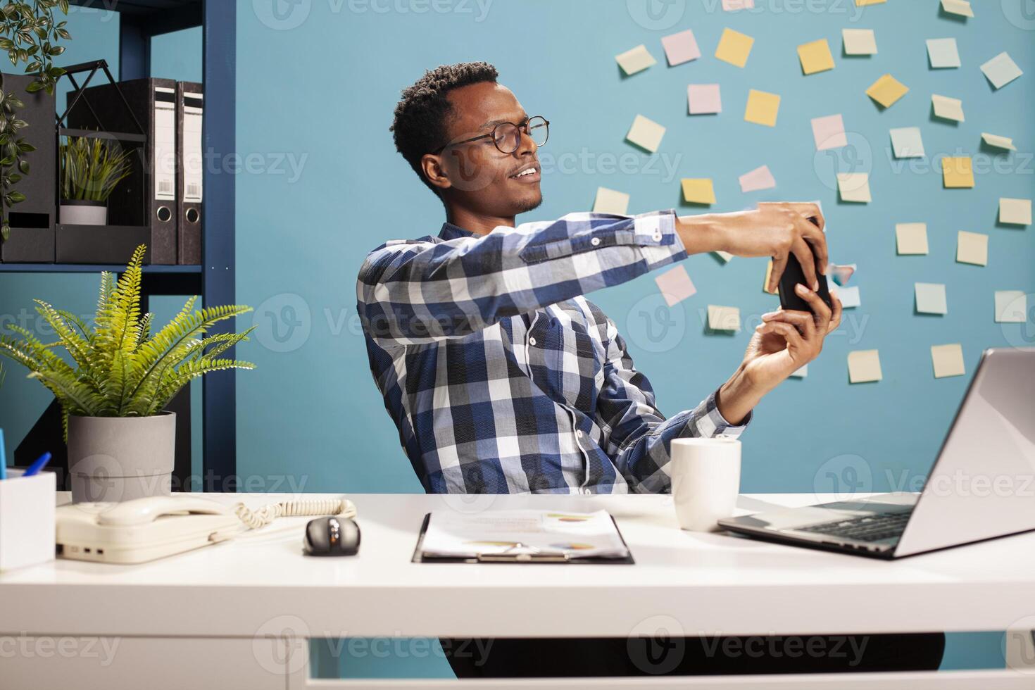 Startup project team leader sitting at his office desk and enjoying a videogame on his smartphone. Young black professional focused on his mobile device, immersed in gaming at his workspace. photo
