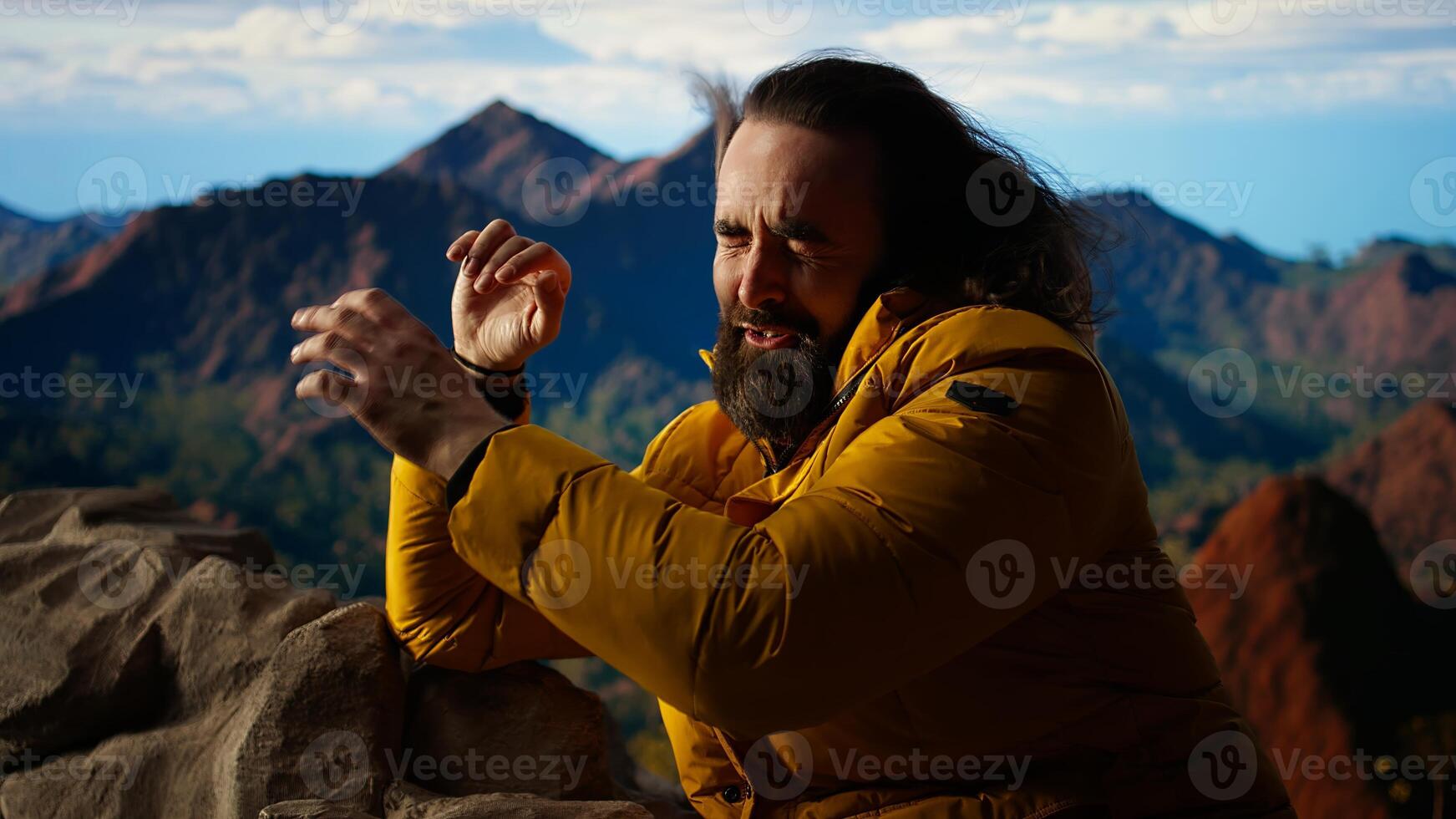 Male active trekker admiring the beautiful mountain range valley but dealing with cold winds, struggling with dangerous windy weather in his campsite. Wanderlust in nature. Camera A. photo