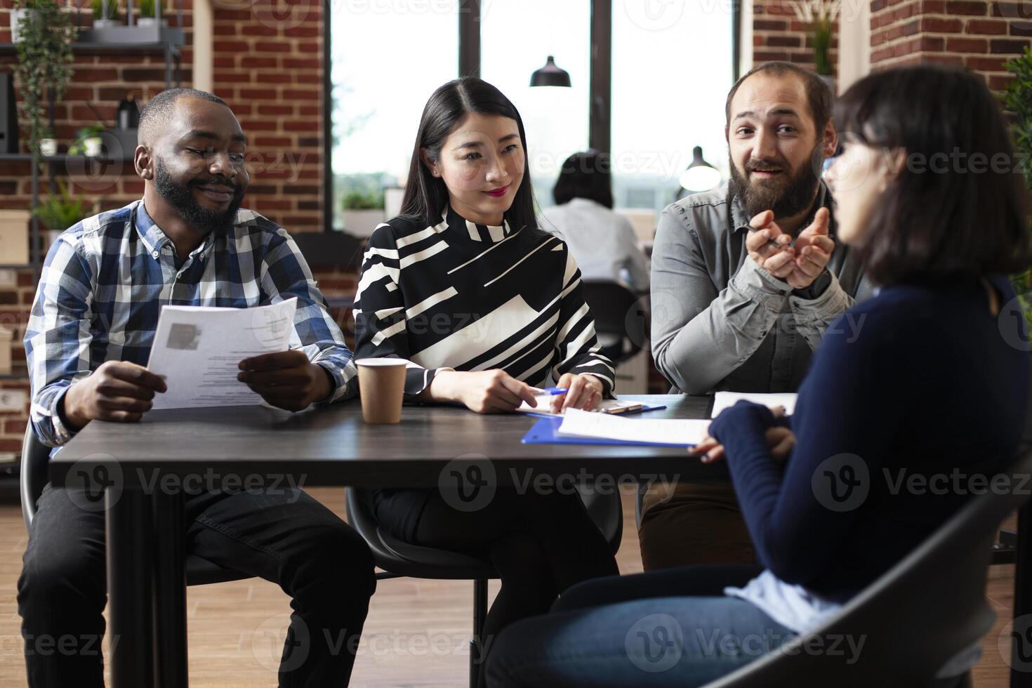 Friendly multiracial HR managers interviewing female candidate at a table, asking about her experience. Diverse recruitment team discussing with potential job applicant. Hiring concept. photo